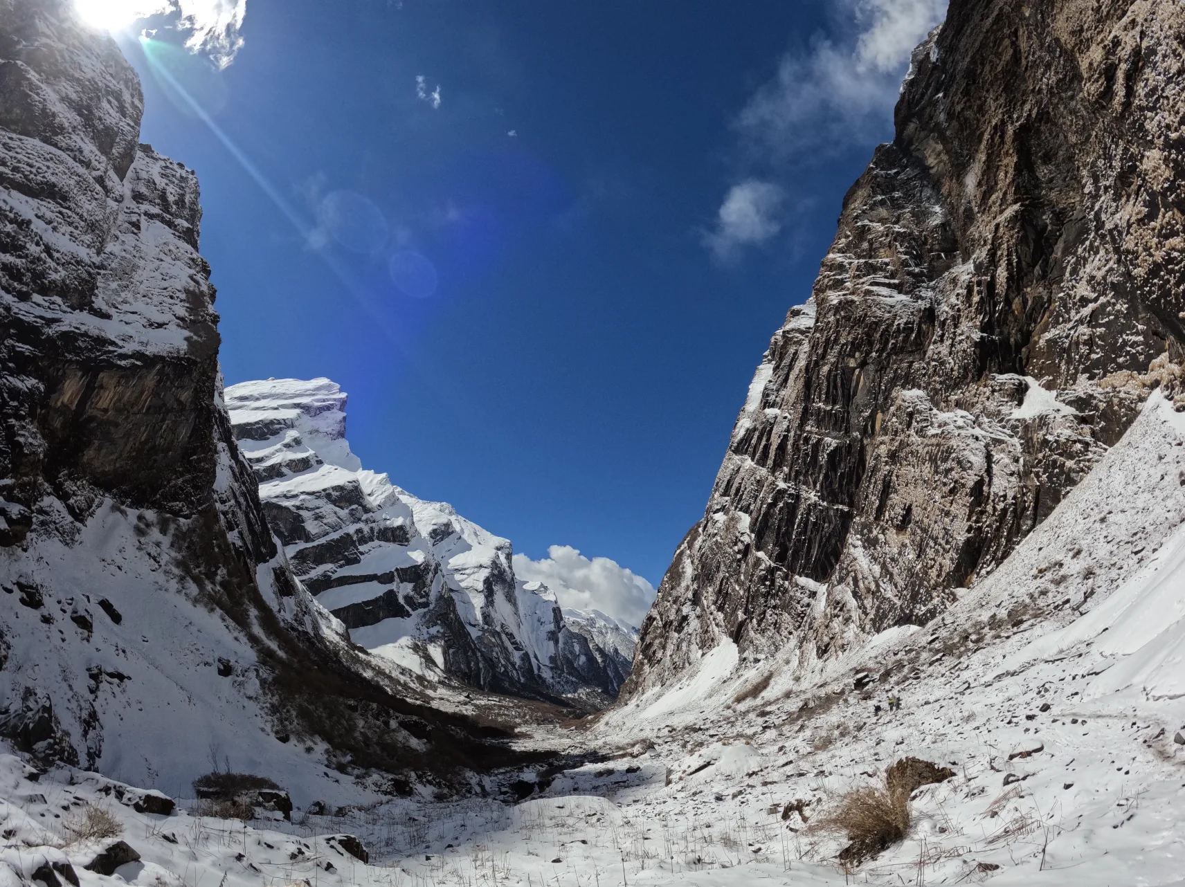 A snow-walled valley in the Nepali Himalayas, sun overhead and a peak rising at the far end.