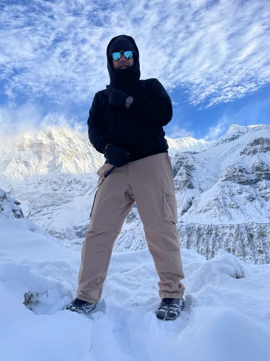 Standing in winter gear on a snow ridge with Himalayan peaks behind.
